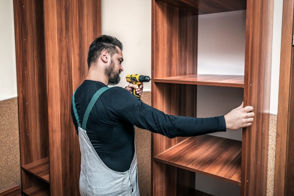 Furniture assembly professional using a power drill to secure a wooden bookshelf