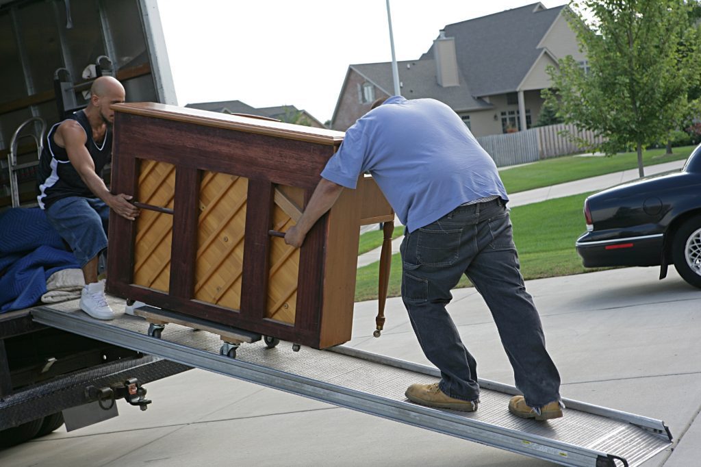 Two professional movers carefully loading a piano onto a moving truck for safe transport