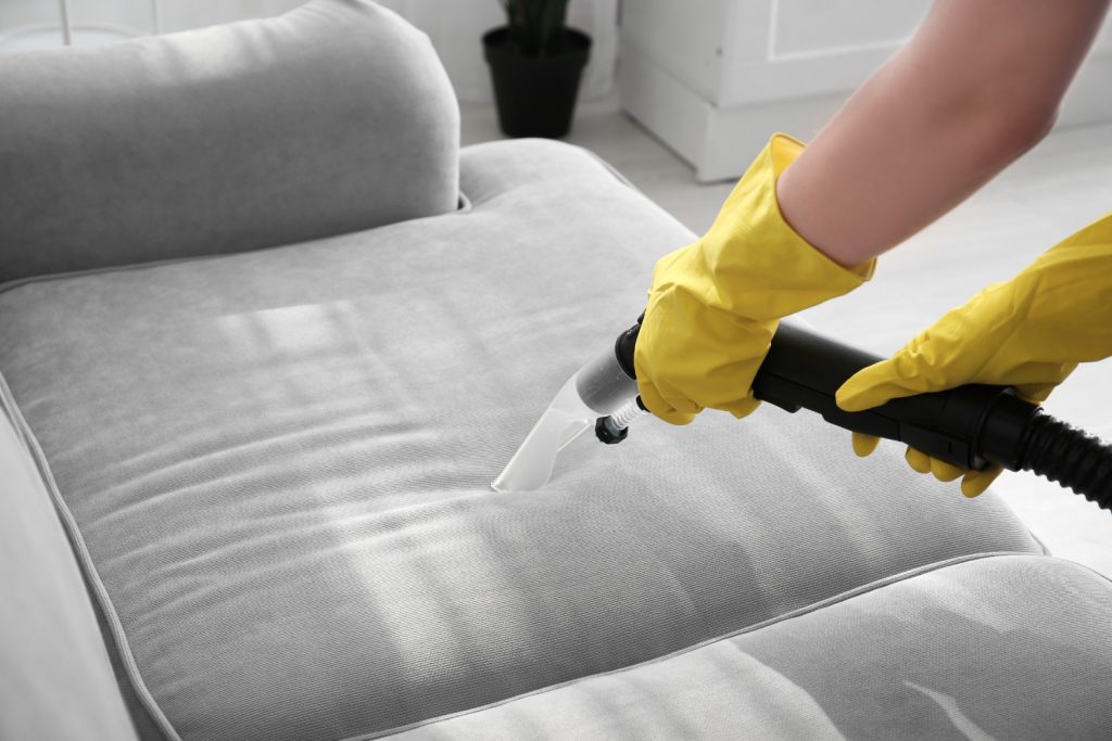 Professional cleaner using a vacuum to deep clean a sofa during upholstery cleaning services in Philadelphia