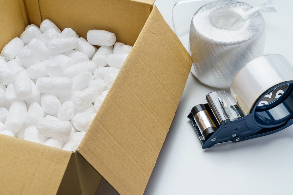 Open cardboard box with packing peanuts, stretch wrap, and tape dispenser for packing services in Delaware County