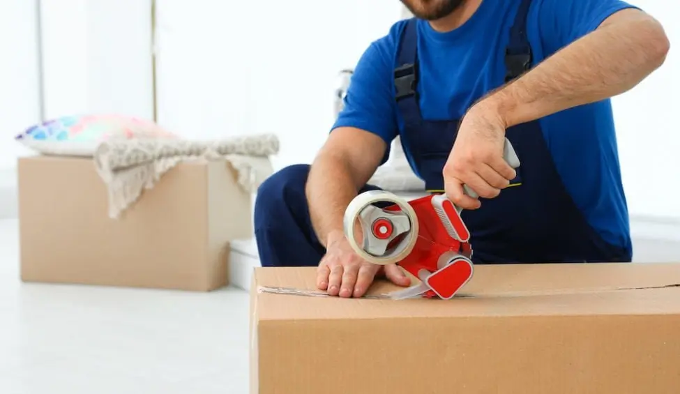 Professional mover sealing a cardboard box with tape during a packing service in Delco