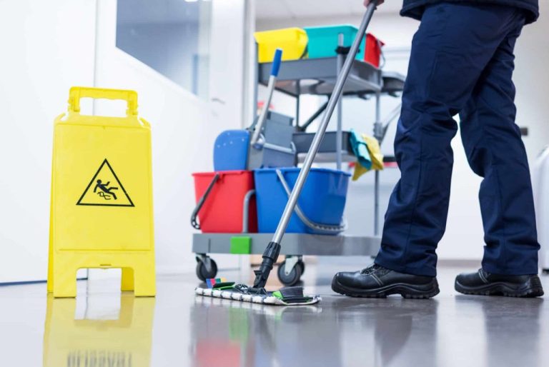 Janitorial staff cleaning and mopping commercial office floors with caution sign