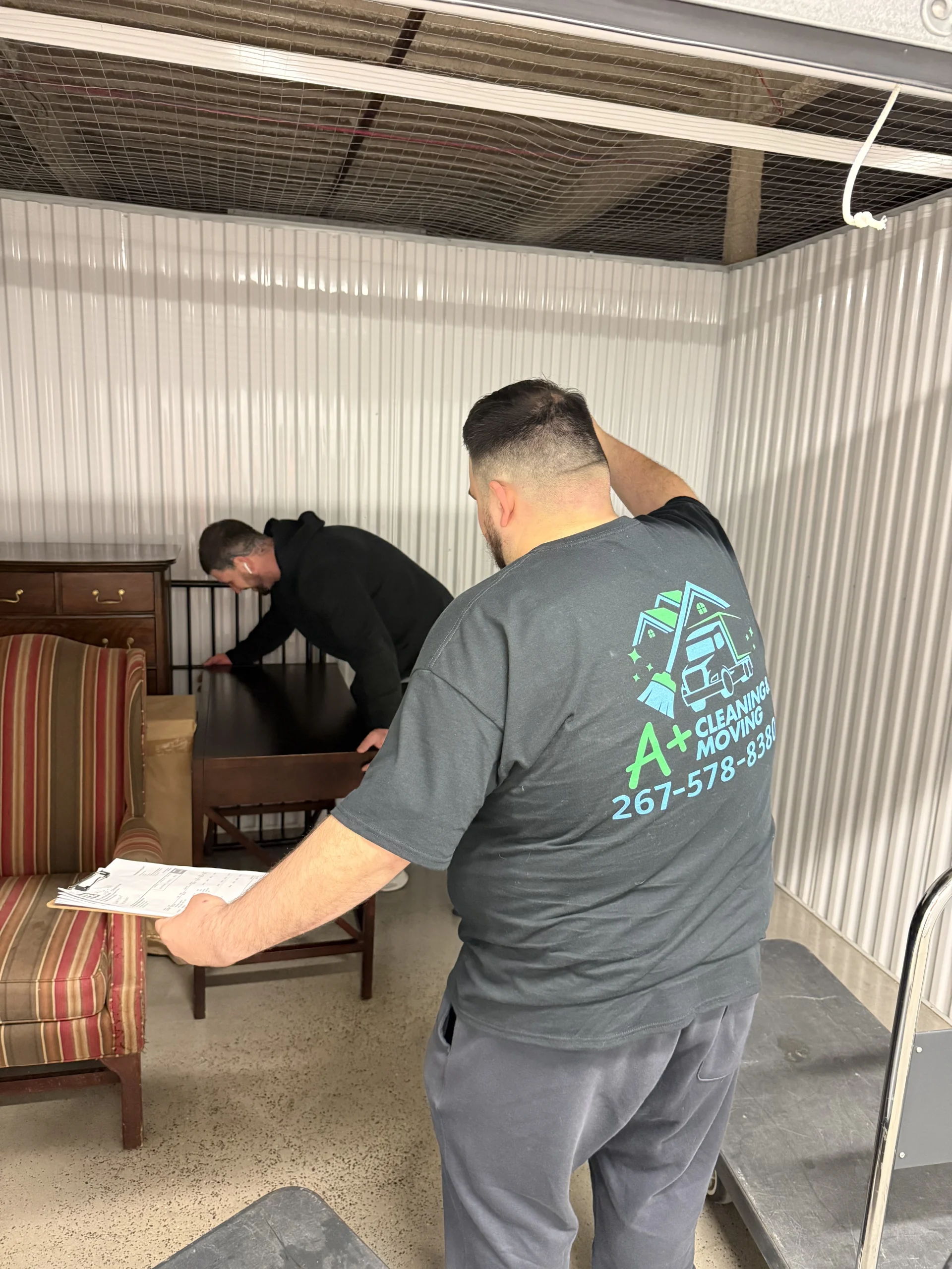 Local movers carefully lifting table into storage unit